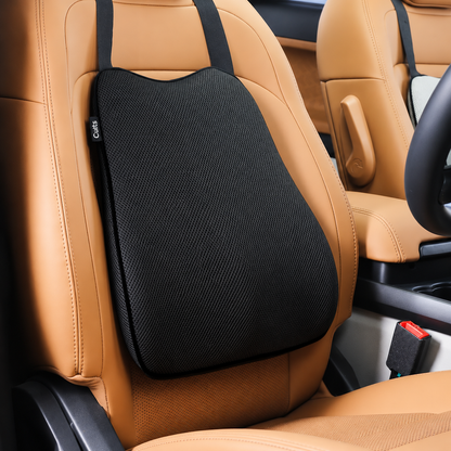 A black car seat back cushion with integrated shoulder straps hanging on a tan leather car seat.