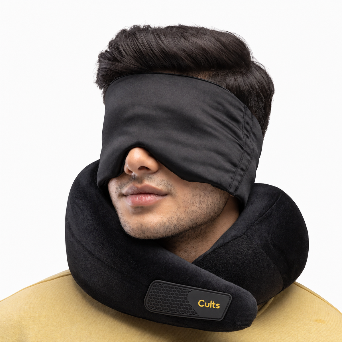 A man wearing a black sleep mask and a black neck pillow with a visible &